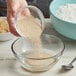 A person pouring red dry yeast into a bowl of flour.