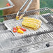 A person using a Mr. Bar-B-Q Stainless Steel Perforated Grill Tray to cook corn on the cob on a grill.