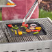 A person using a Mr. Bar-B-Q non-stick grill tray to cook vegetables on a grill.