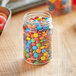 A clear round PET jar filled with colorful candy on a table.
