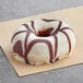 A Europastry white donut with chocolate drizzle on top sitting on paper.