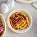 A Tellus Products bagasse plate with hummus and pomegranate seeds on a table.