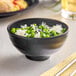 An Acopa Izumi matte black melamine rice bowl filled with rice and peas.
