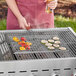 A person using an Outset Chrome Flex Grill Basket to cook food on a grill.