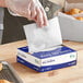 A person in gloves using Choice customizable wax paper to line a box of food.