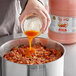 A person pouring orange hot sauce into a pot of food.