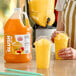 A gallon jug of Carnival King peach slush syrup concentrate next to two cups of yellow peach slushies.