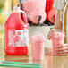 A gallon jug of Carnival King cotton candy slush syrup concentrate next to two cups of pink slushies with dome lids.