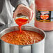 A person pouring Marie Sharp's Belizean Heat Habanero hot sauce into a pot.