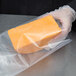 A hand in gloves holds a piece of cheese in an ARY VacMaster vacuum packaging bag.