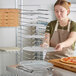 A woman in an apron placing a pizza pan on a GI Metal pizza pan rack.