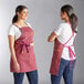 Two women wearing Acopa Hazleton wine canvas bib aprons on a counter in a professional kitchen.