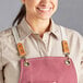 A woman wearing a pink Acopa canvas bib apron with brown straps.