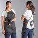 Two women wearing Acopa Hazleton black canvas cross-back bib aprons in a professional kitchen.