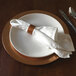 A white Tabletop Classics by Walco plastic charger plate with silverware on it.