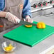 A person uses a Choice green polyethylene cutting board to cut a yellow bell pepper.