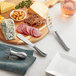 An Acopa stainless steel cheese knife set on a cutting board with cheese, meat, and bread.