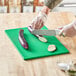 A person cutting eggplant on a green Choice cutting board.