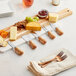 An Acopa cheese board with cheese knives and forks on a table with various types of cheese and fruits.