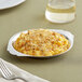 A stainless steel round au gratin dish filled with macaroni and cheese on a table with a fork.
