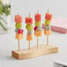 A wooden Acopa Mesa skewer holder with fruit on sticks.