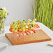 An Acopa dark brown wood skewer holder with shrimp and fruit skewers on a plate.
