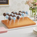 An Acopa dark brown wood skewer and cake pop holder with cake pops on a table.