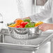 A person washing vegetables in a metal Choice stainless steel colander.