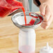 A person using a Choice stainless steel wide mouth funnel to pour red juice into a plastic container.