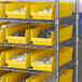 A metal shelf rack with yellow Regency plastic bins filled with white and grey items.