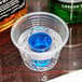 A Fineline Quenchers plastic shot cup filled with blue liquid on a bar table.