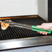 A person holding Vollrath Jacob's Pride tongs with a green Kool Touch handle over a grill.