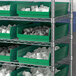 A shelf with Regency green plastic shelf bins filled with white objects.