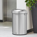 A Rubbermaid stainless steel half round waste container next to a plant.