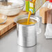 A person pouring orange juice from a carton into a metal measuring cup with a handle and pour lip.