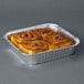 A 8" square foil cake pan with cinnamon rolls in it.