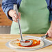 A person using a Choice stainless steel ladle to put red sauce on a pizza.