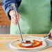 A person using a Choice stainless steel ladle to put red sauce on a pizza.