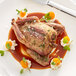 A white plate with a whole cooked squab with head and feet on, served with sauce and vegetables.