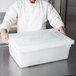 A chef in a white coat placing a Rubbermaid white plastic lid on a large container.