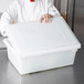 A chef holding a white plastic container with a white lid.