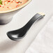 An Acopa Ugoki matte black soup spoon with ivory accents in a bowl of soup.