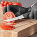 A person in black gloves using a Schraf serrated tomato knife to cut a tomato.
