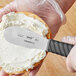 A person using a Schraf sandwich spreader to spread cream cheese on a bagel.