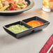 An Acopa matte black melamine sauce dish with ivory rim holding two sauces on a table.