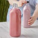 A person holding a 59 oz square PET clear bottle of pink liquid.