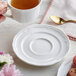 A person holding a cup of tea with an Acopa Condesa scalloped porcelain saucer.