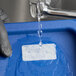A dissolvable product label being washed off a blue container under running water.