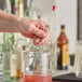 A person using a Choice bar spoon with a red knob to mix a drink in a glass.