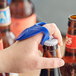 A person uses a Franmara blue plastic knuckle bottle opener to open a beer bottle.